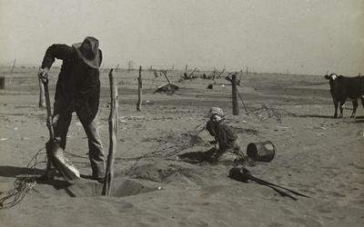 Dust bowl farmer raising fence to keep it from being buried under drifting sand in Cimarron County, Oklahoma.