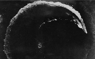 Black and white image of a Japanese battleship circling to avoid a US air attack in the Pacific.