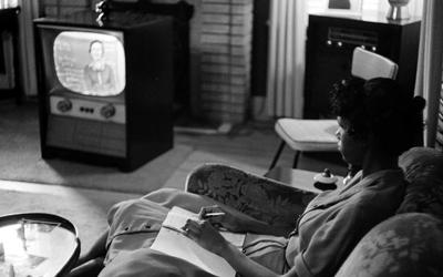 A high school student sits in her living room watching her television which plays an educational course. 