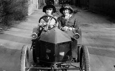 Two children ride in an early model of the automobile.