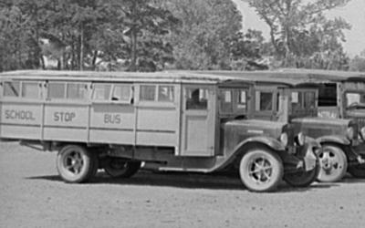 This image shows a line of parked motorized school buses that were used in the early twentieth century. 