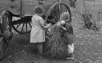 This image shows two children playing with dolls in the tumbleweed on a farm during the Great Depression. 