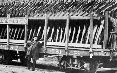 Photograph shows three men and a railroad car loaded with steel plows.  Article tells a brief narrative of Mr. John Deere.