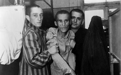 The image shows a very thin and sick looking man who is the victim of the holocaust.  He is with two men who are holding him up.