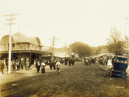 Hundreds of fairgoers walk the unpaved Grand Avenue next to a Dodd and Struthers Lightning Rods building
