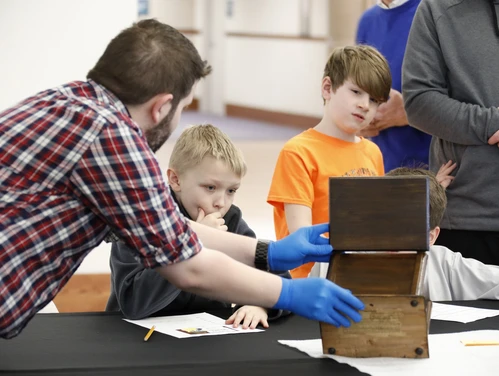 A museum staff member shows a historical artifact to a young learner