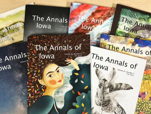 Pile of past issues of The Annals of Iowa with the covers featuring artwork by Iowa artists