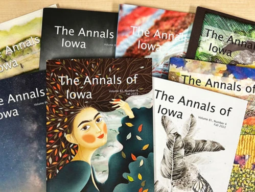 Pile of past issues of The Annals of Iowa with the covers featuring artwork by Iowa artists