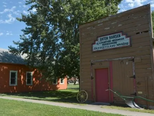 Exterior of a historic blacksmith shop with a horse-drawn plow sitting by the front door