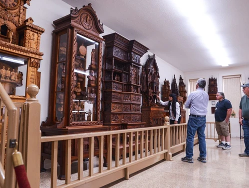 Several visitors gaze at a wall lined with wood clocks intricately carved by the Bily brothers