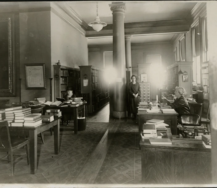 View of reading room and library stacks with employees and the public at the old State Historical Building in Des Moines circa 1920.