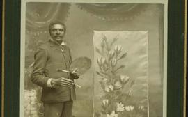 George Washington Carver stands beside a painting holding a paintbrush.