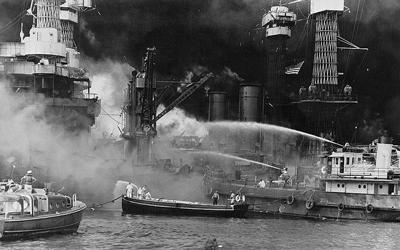 The black and white image shows the aftermath of the bombing of Pearl Harbor, Hawaii with the  USS West Virginia aflame.