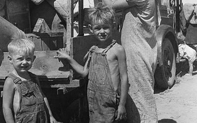Black and white photograph of a mother and two sons behind a truck filled with their possessions.  