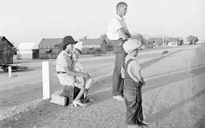 This image shows a family of three - father, mother and young son - waiting on the side of the road.  According to the title, they are relocating to California.
