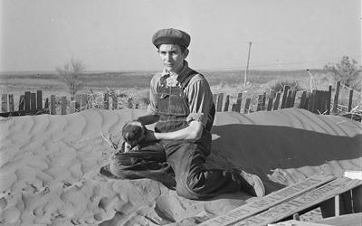Image shows a young boy holding what appears to be a football sitting on top of a very large dune of dust.  It looks like he is sitting on a sand dune in a desert.