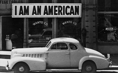 A large sign reading "I am an American" placed in the window of a store in a black and white image.