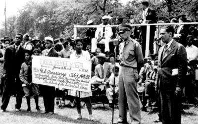 The image shows a crowd presenting a large check to the military in Chicago.