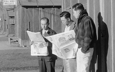 Black and white image three men, two reading newspapers, standing in front of Office of Reports, Free Press.