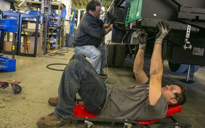 Assembly line workers Jared Maas, right, and Stan Trca work under the chassis of an RV on the Winnebago Industries assembly line in Forest City in March 2016.