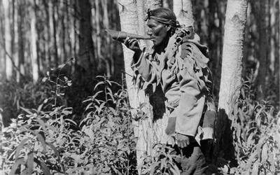 A Northwest Native American man, a member of the Cree tribe, in the woods calling a moose with a blowing horn. 