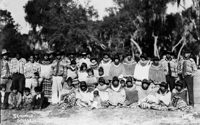 Seminole men, women and children are posing outdoors.