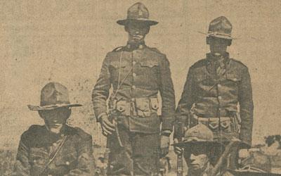 The black and white image shows five soldiers standing around a machine gun.  
