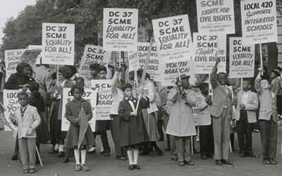 The black and white photograph depicts a racially diverse group of women and children protesting for integrated schools.  
