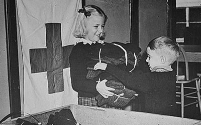 Image shows two young kids at the Red Cross in Des Moines, IA packing clothing for refugees during World War Two.