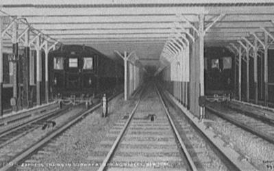 Three subway tracks visible along with many structural support poles.  One inbound and one outbound subway train are visible.