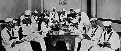 Picture of African-American soldiers and sailors sitting and standing around a table in a Red Cross Rest Room specifically outfitted for only African Americans during World War I.
