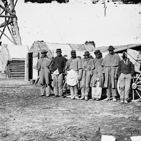 One of the Civil War photographs compiled by Hirst D. Milhollen and Donald H. Mugridge, this 1864 image depicts seven “contraband” teamsters dressed in old Union uniforms standing near a wagon and shack.  