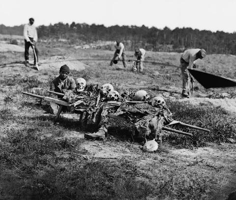 This photograph, published by John Reekie in April 1865, portrays five African-Americans collecting bones of soldiers killed in battle during Ulysses S. Grant’s 1864 Virginia Overland Campaign. In the foreground an African-American squats near a stretcher filled with skulls, bones, and decaying limbs. 