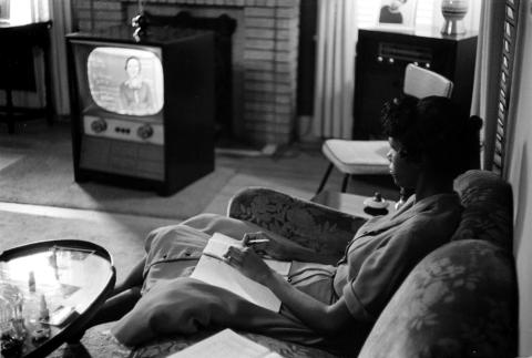 A high school student sits in her living room watching her television which plays an educational course. 