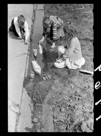 Three children play outside with toy boats in the town of Grundy Center, Iowa. 