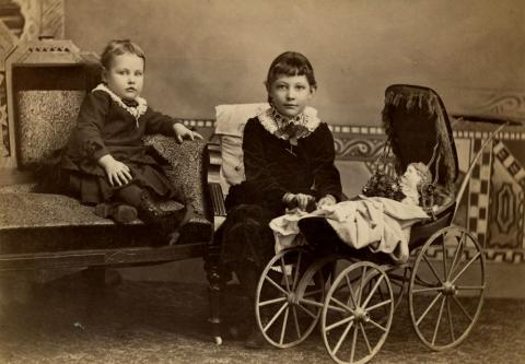 Photograph portrait of two girls with doll in baby buggy in Shendandoah, Iowa. 