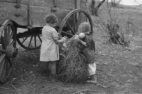 This image shows two children playing with dolls in the tumbleweed on a farm during the Great Depression.