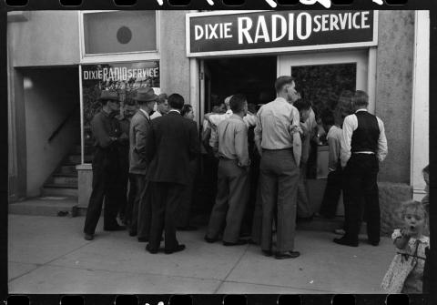A crowd of men gather outside a radio shop to listen to the World Series game. 