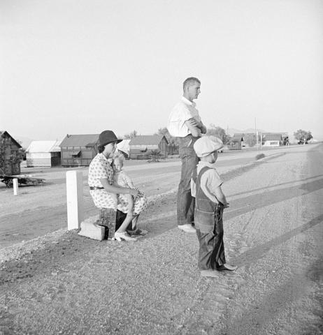 This image shows a family of three - father, mother and young son - waiting on the side of the road.  According to the title, they are relocating to California.