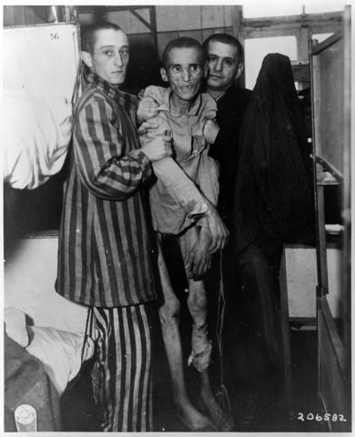 The image shows a very thin and sick looking man who is the victim of the holocaust.  He is with two men who are holding him up.