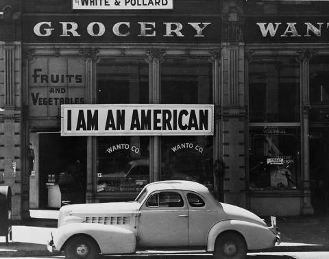 A large sign reading "I am an American" placed in the window of a store in a black and white image.