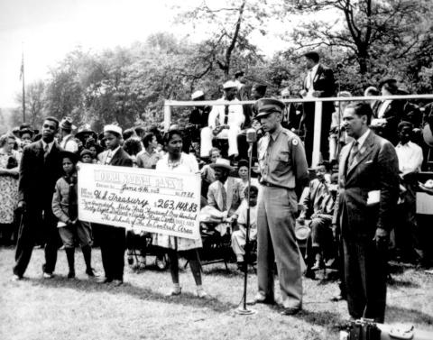 The image shows a crowd presenting a large check to the military in Chicago.