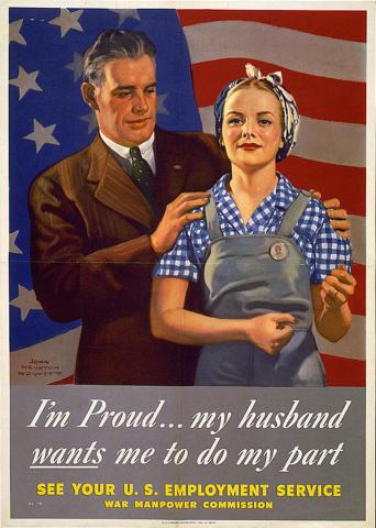 Husband, in suit, and wife in working clothes, standing in front of U.S. flag.