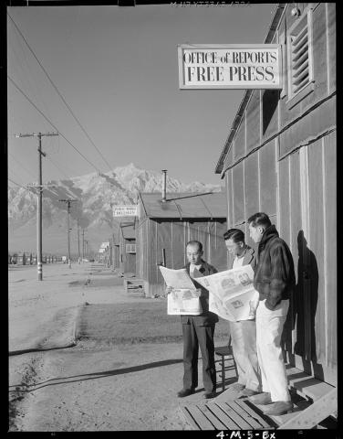 Black and white image three men, two reading newspapers, standing in front of Office of Reports, Free Press.