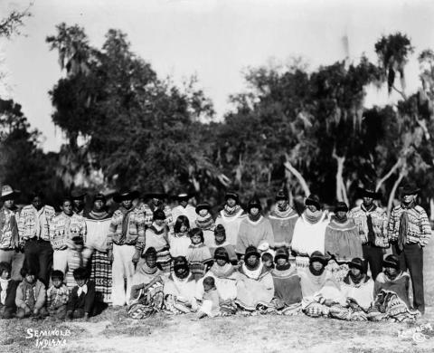 Seminole men, women and children are posing outdoors.