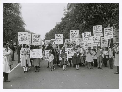 The black and white photograph depicts a racially diverse group of women and children protesting for integrated schools.  