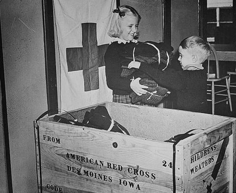 Image shows two young kids at the Red Cross in Des Moines, IA packing clothing for refugees during World War Two.