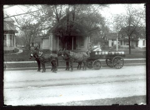 Horse-drawn wagon filled with milk cans in a residential section of Des Moines.