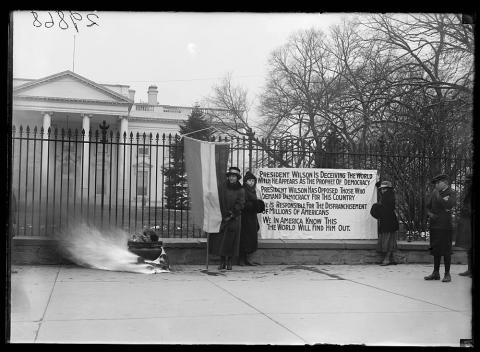 In this 1918 photograph taken by Harris & Ewing, two suffragettes hold a banner outside the gates of the White House accusing President Woodrow Wilson of hypocrisy when he claims to fight for and support democracy during World War I, all the while denying women the right to vote in his own country.