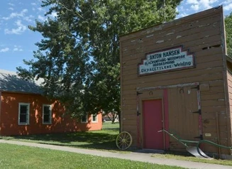 Exterior of a historic blacksmith shop with a horse-drawn plow sitting by the front door